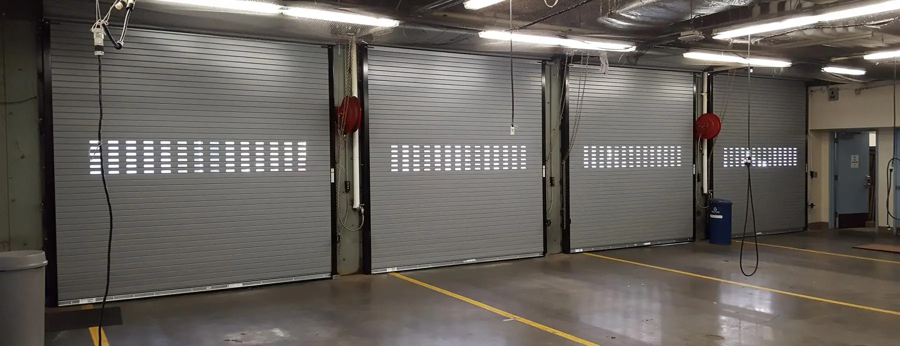 Four ordinary rolling steel doors seen from inside a row of service bays