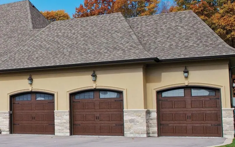 House with three wood-look garage doors and autumn trees behind it