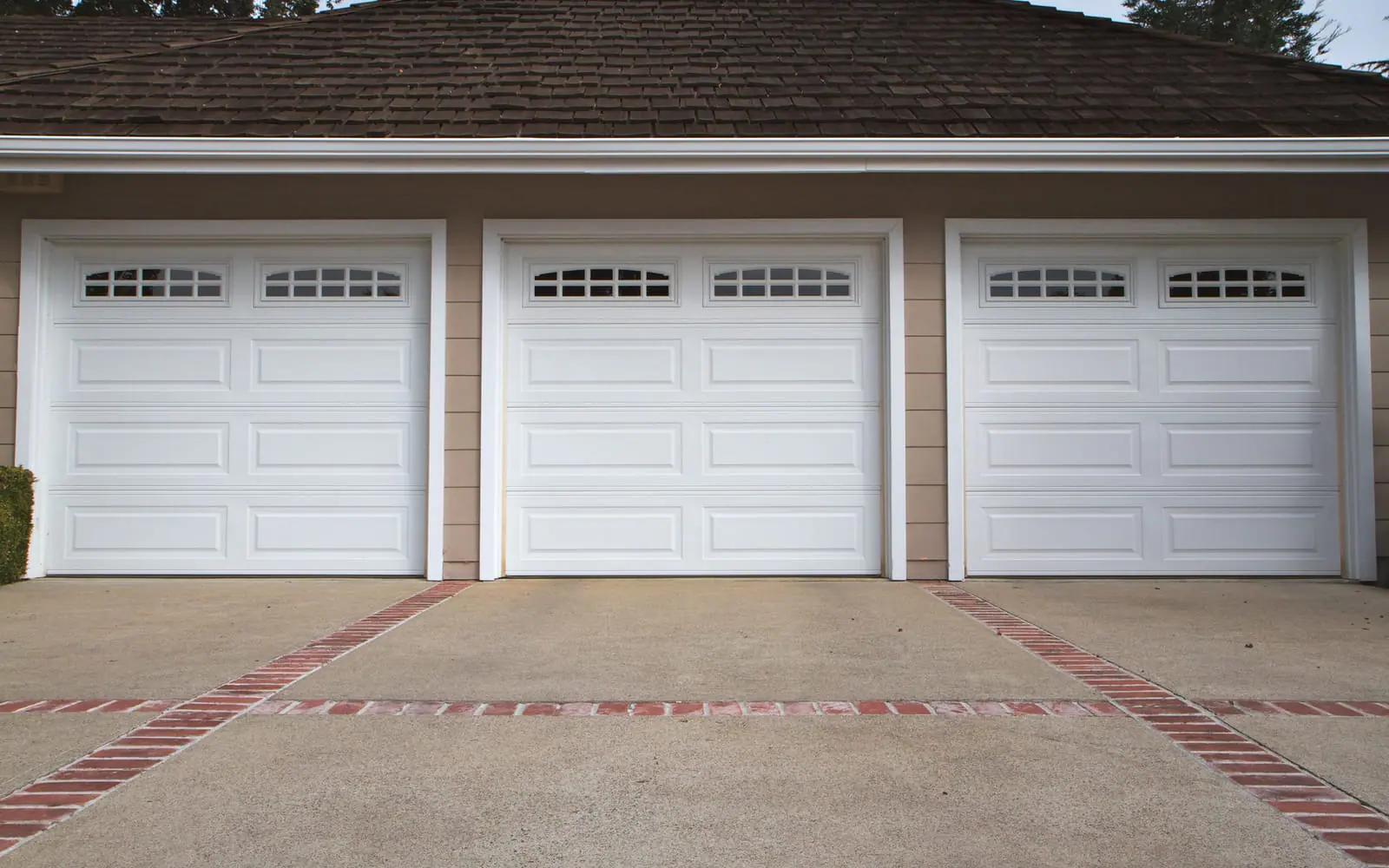 Three white garage doors with window rows on one building