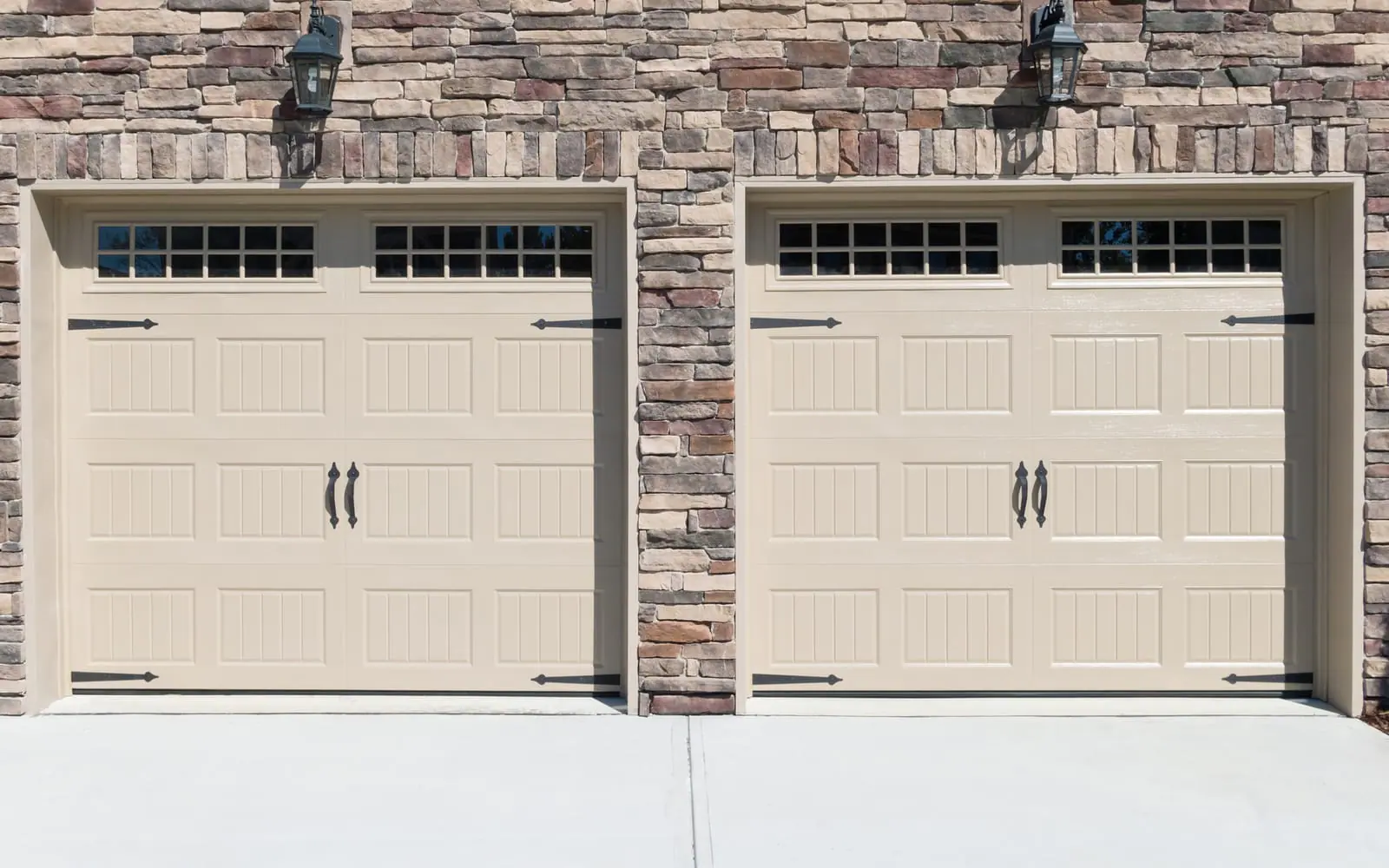 Two tan carriage-style garage doors set in a stone wall