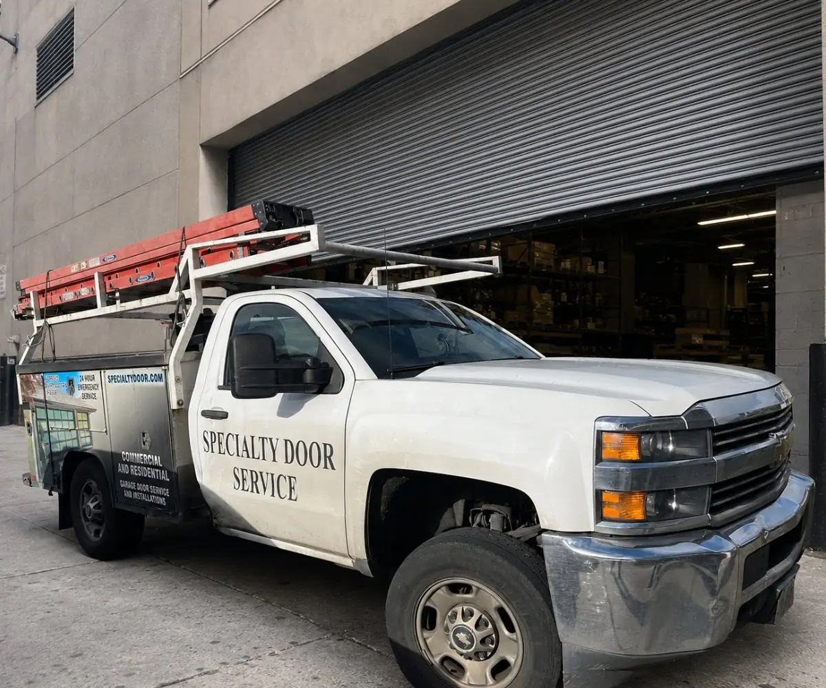 Specialty Door Service truck with ladders parked at a large rolling steel door