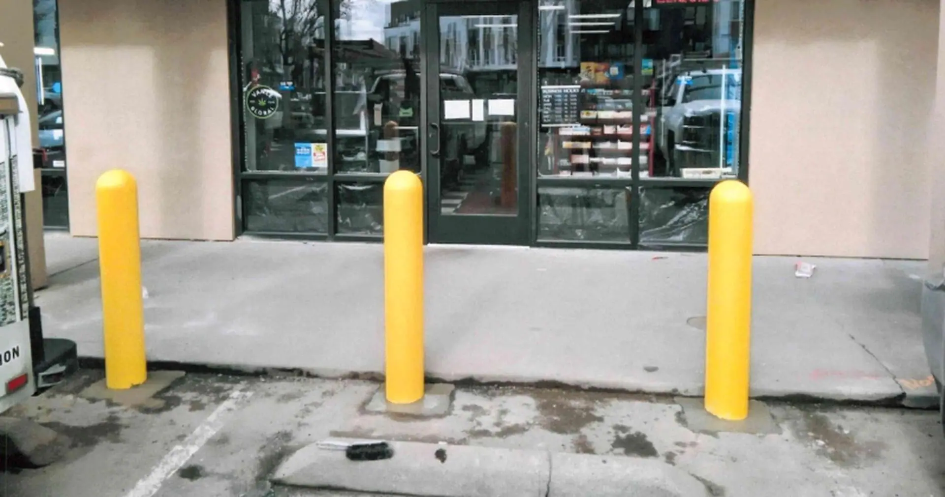 Three yellow bollards in front of a glass storefront entrance