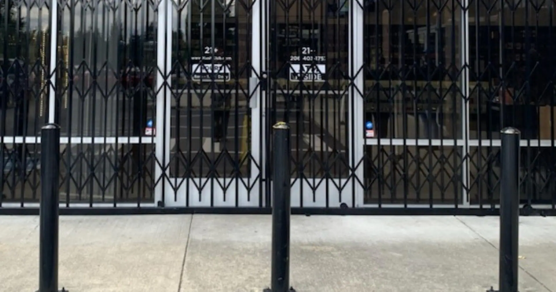 Folding security gates closed across a storefront, with bollards in front