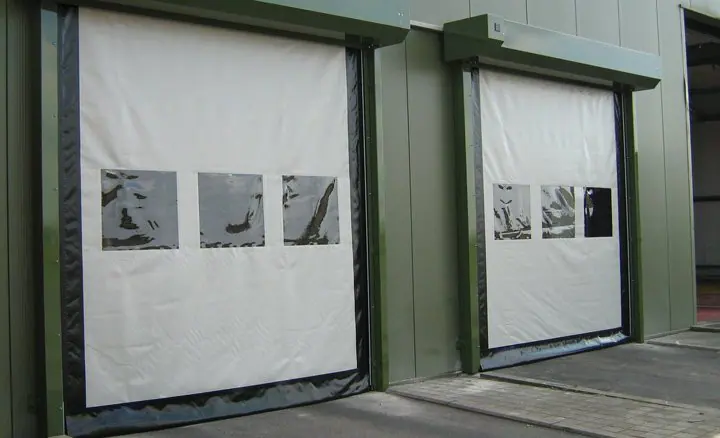Two white high-speed fabric doors with vision panels on a green metal building