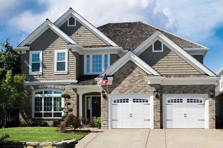 Brick and shingle home with two white carriage-style garage doors