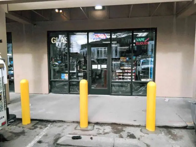 Three yellow bollards on the walk in front of a glass storefront
